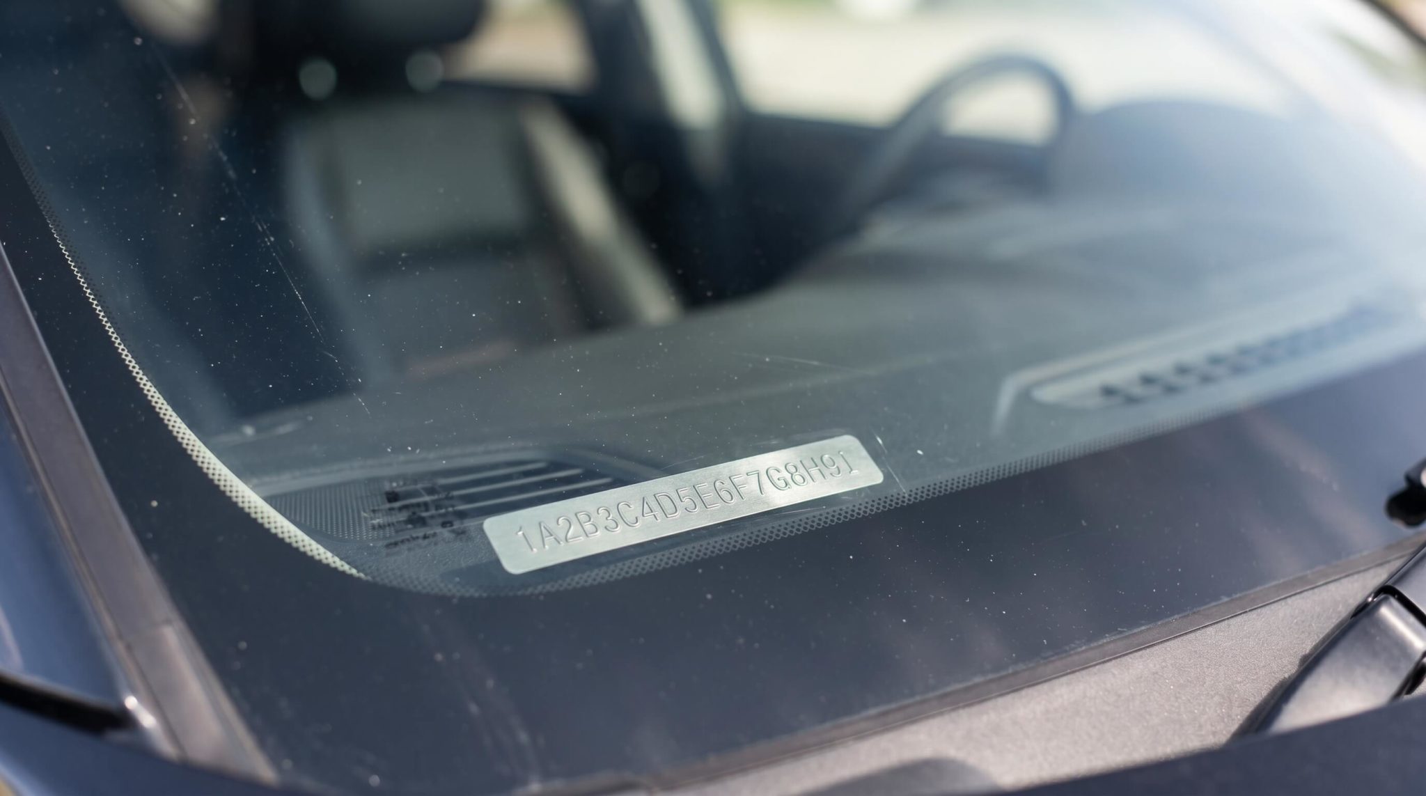Close-up of a 17-character VIN plate on a vehicle dashboard at the base of the windshield